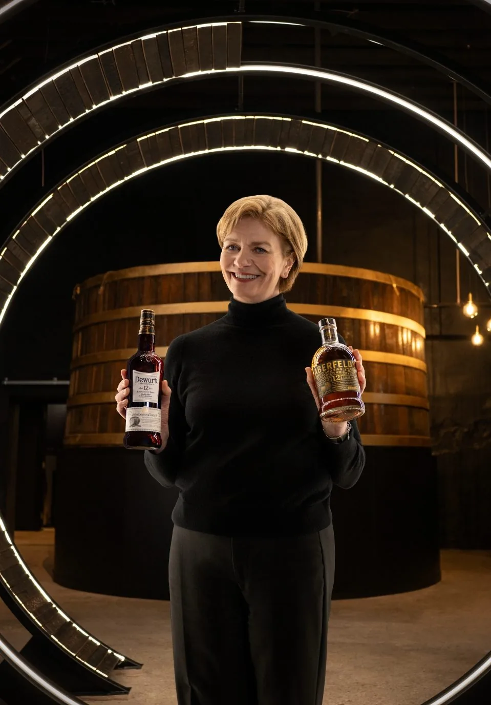 A photo of Stephanie Warehouse holding two bottles of Dewars. Dewar’s Aberfeldy Distillery - immersive experience studio